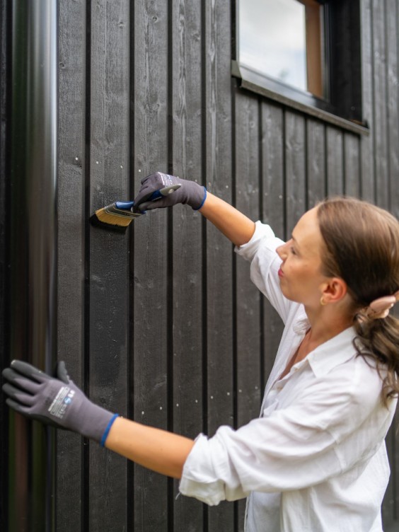 sieviete krāso koka fasādi melnā tonī