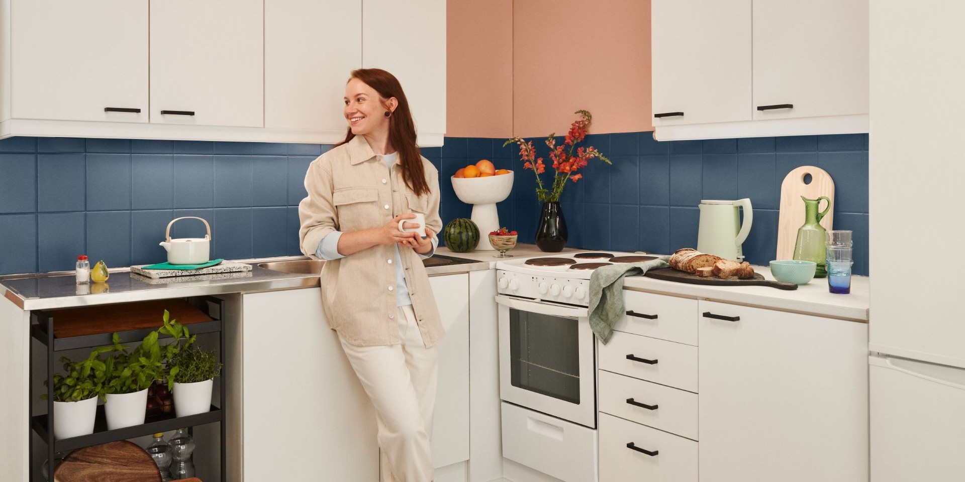 woman in white kitchen with blue backsplash and peach colour wall