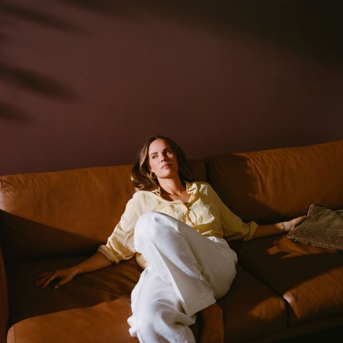 woman relaxing on brown leather sofa and warm brown wall colour in background