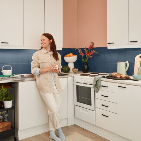 woman in white kitchen with blue backsplash and beige wall